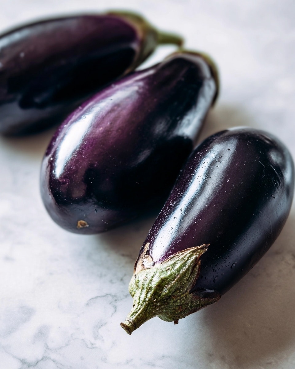 Three whole eggplants are placed on a white marbled surface. They are shiny and dark purple with smooth skin. Two eggplants lie horizontally at the back, and one eggplant is front and center, showing its greenish-brown stem and slightly rough cap. The lighting highlights the reflections on the eggplants’ skins, showing their smooth texture. Photo taken with an iphone --ar 4:5 --v 7