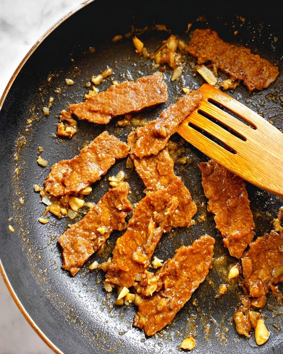 The image shows a close-up of a black frying pan with several thick, uneven slices of brown textured food cooking in oil. The pieces have a slightly shiny look, coated with bits of light-colored chopped garlic or similar small fragments that are mixed and scattered around. A wooden slotted spatula rests on the right side of the pan, partly touching some of the slices. The frying pan’s surface has a non-stick textured appearance with some shiny oil spots reflecting light. The photo is taken on a white marbled surface. photo taken with an iphone --ar 4:5 --v 7