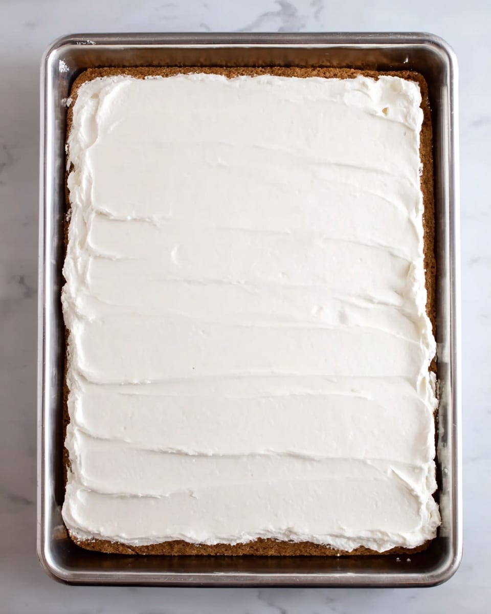 A large rectangular cake with three visible layers is displayed in a shiny metal baking tray. The bottom layer is a light brown cake base, textured and firm. The middle and top layers are thick, smooth, and evenly spread white frosting, covering the entire surface. The edges of the frosting layer are slightly rough but mostly flat, showing the clean contrast between the cake and the frosting. The tray is placed on a white marbled surface. Photo taken with an iphone --ar 4:5 --v 7