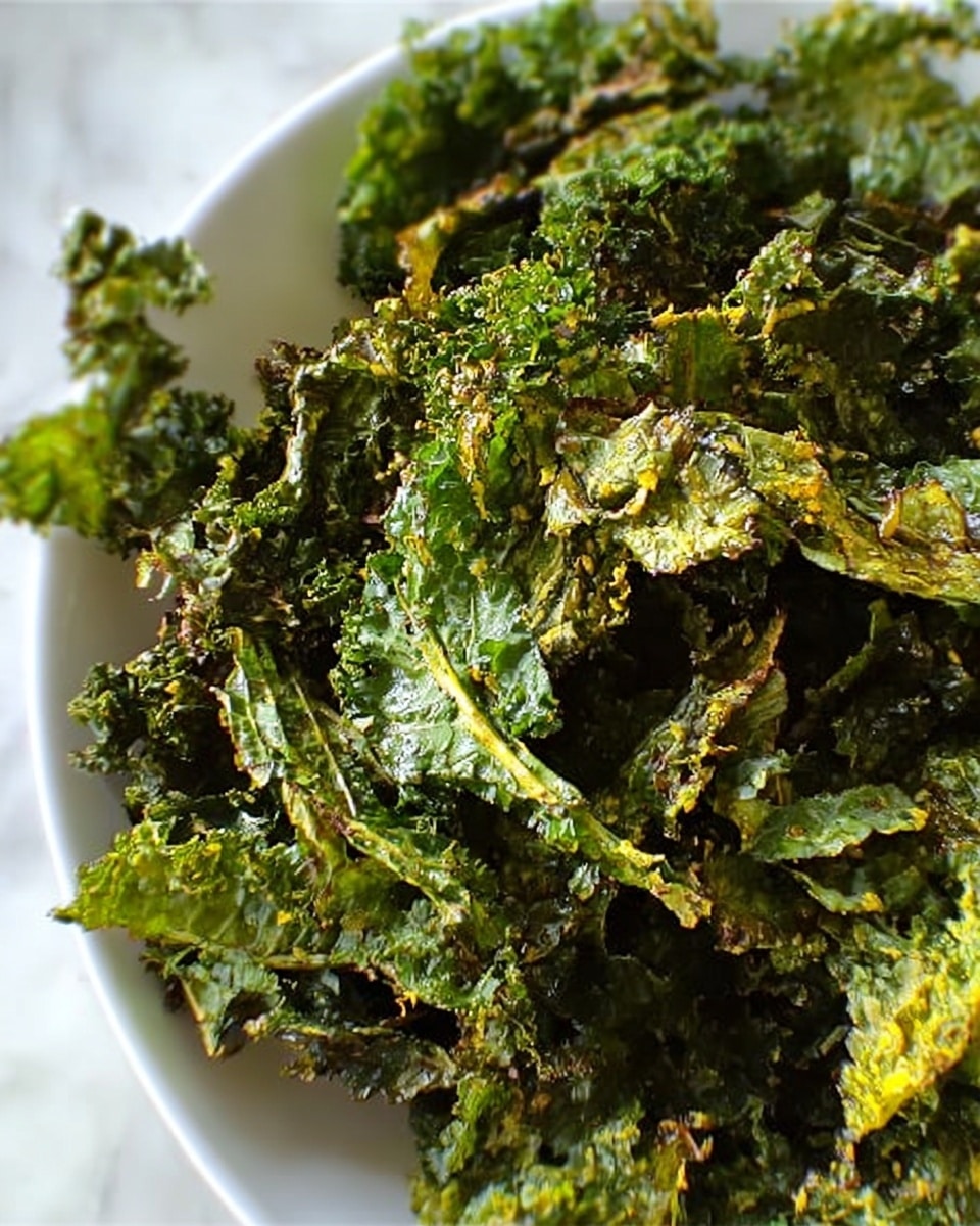 A close-up image showing a white plate filled with many crispy kale chips that are green with some parts showing slight yellowish-brown spots from cooking. The kale chips have a rough, wrinkled texture and are layered unevenly, giving a sense of crunchiness. The background is a white marbled surface. photo taken with an iphone --ar 4:5 --v 7