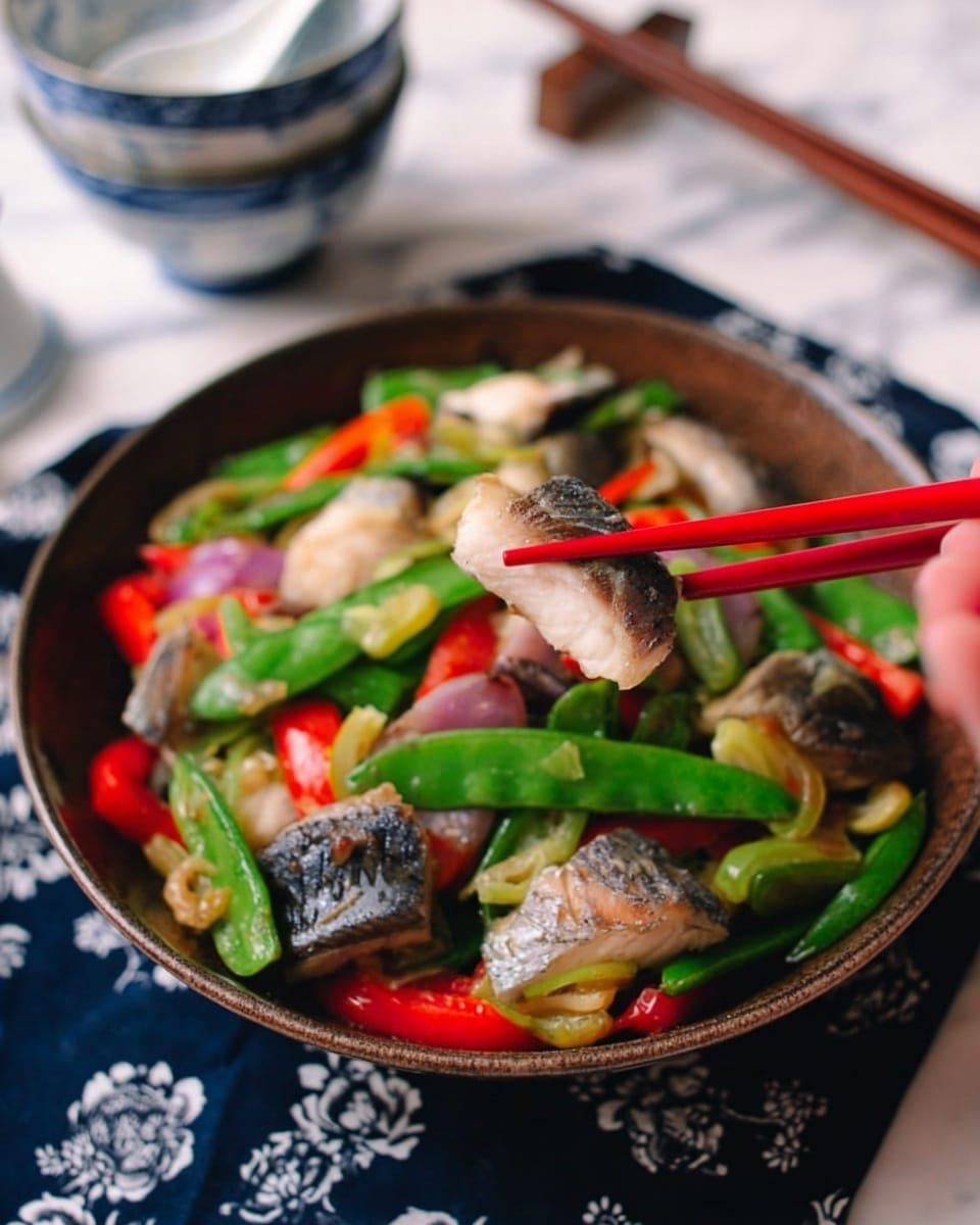 The image shows a brown bowl filled with a colorful stir-fry dish placed on a white marbled surface over a dark blue cloth with white floral patterns. The dish has pieces of white fish with dark skin on one side spread throughout, vibrant green snap peas, bright red bell pepper chunks, and small pieces of purple onion creating a mix of colors and textures. A pair of red chopsticks held by a woman's hand is lifting a piece of white fish from the bowl. In the blurred background, there are three stacked white bowls with blue designs and two white spoons inside the top bowl. The overall look is fresh, vibrant, and appetizing, photo taken with an iphone --ar 4:5 --v 7