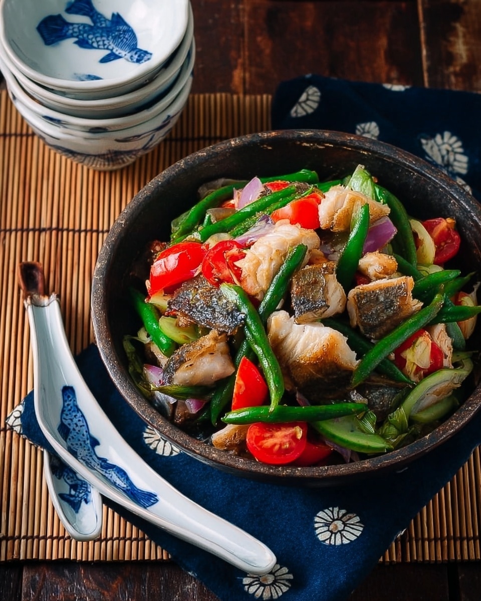 A bowl filled with a mix of cooked fish pieces showing white and brown skin textures on top, green snap peas, sliced green beans, bright red chopped tomatoes, and small chunks of purple onion, all layered together creating a colorful and fresh look. The bowl is dark with a rustic feel and sits on a dark blue cloth with small white flower prints, placed over a bamboo mat on a dark wooden table. Next to the bowl, there are stacked white bowls with blue fish patterns inside, holding two white ceramic spoons with the same blue fish design. The whole setting is on a white marbled surface. photo taken with an iphone --ar 4:5 --v 7