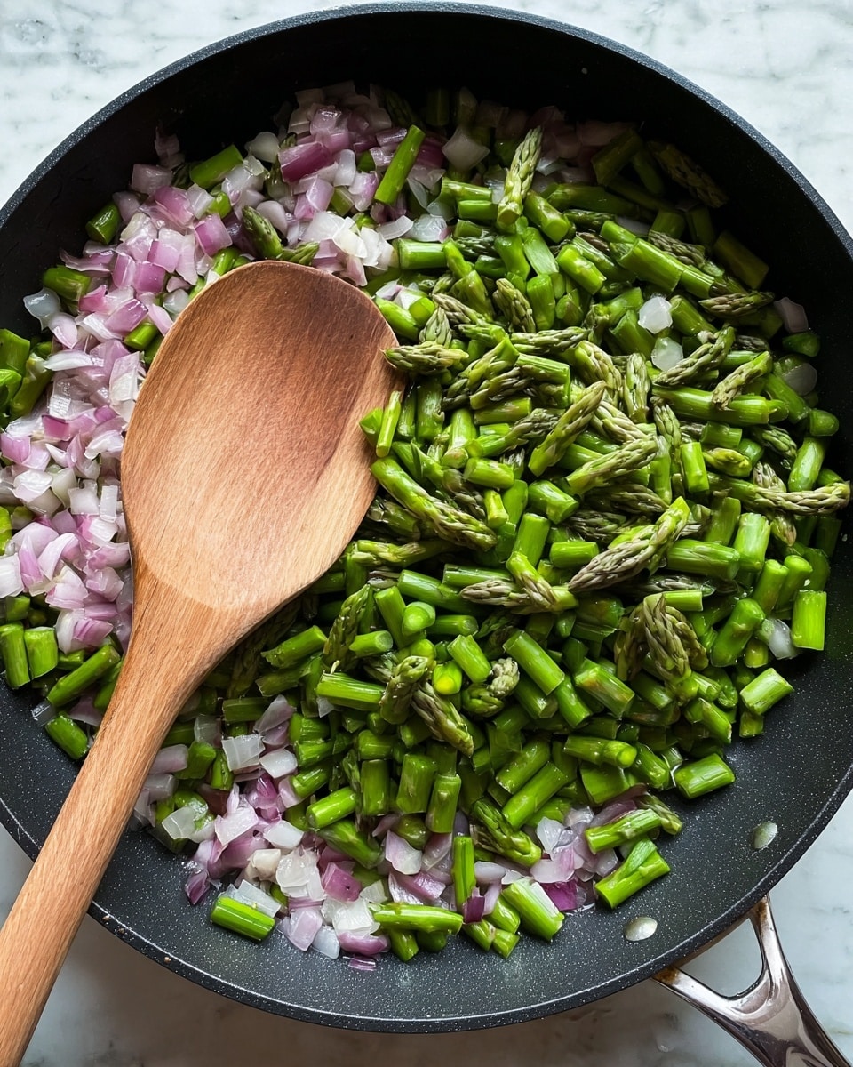A black pan filled with two layers of food: the bottom layer is small diced pieces of onion with a light purple and white color, and the top layer consists of chopped green asparagus pieces, some showing their light green tips. A large wooden spoon with a smooth texture rests lightly on top of the vegetables, angled towards the left side. The pan handle is visible at the bottom right corner, and the whole setup is placed on a white marbled surface. photo taken with an iphone --ar 4:5 --v 7