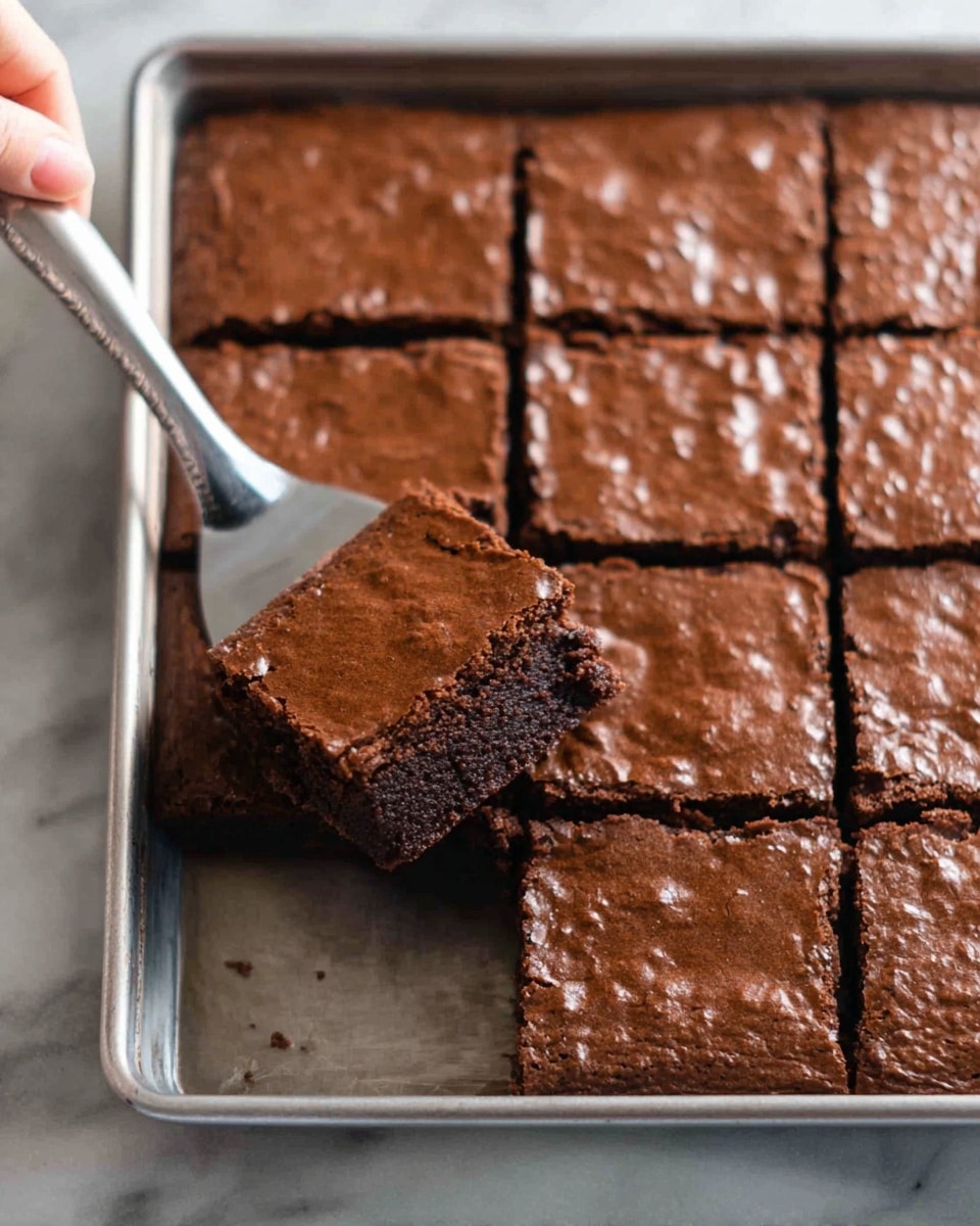 A close-up of a metal baking tray filled with nine square chocolate brownies arranged in three rows. Each brownie has one smooth, slightly cracked top layer with a shiny chocolate surface. One square brownie is lifted by a woman's hand holding a metal spatula, showing the brownie’s moist, dark brown, dense texture underneath. The tray sits on a white marbled surface. photo taken with an iphone --ar 4:5 --v 7