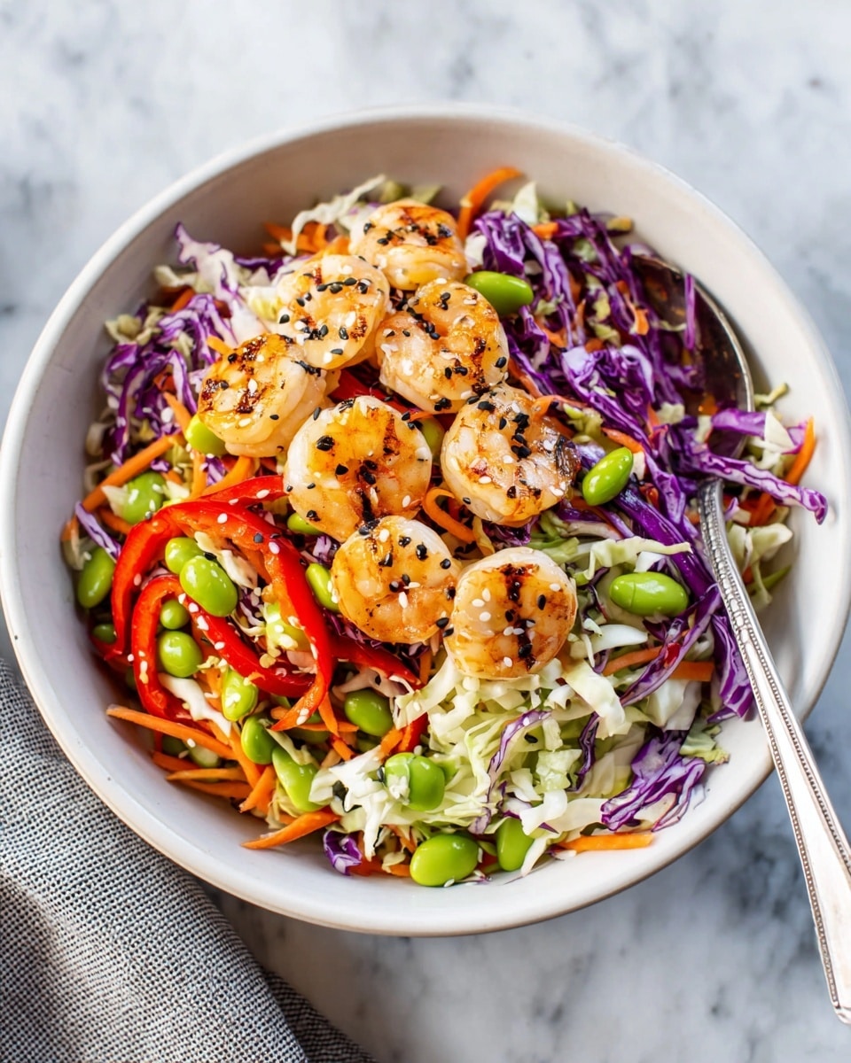A white bowl filled with a colorful salad showing three main layers is on a white marbled surface. The bottom layer is a mix of shredded white and purple cabbages. The middle layer has thin strips of orange carrots, bright green edamame beans, and red bell pepper slices, adding vibrant color. The top layer has grilled shrimp, each piece light orange with dark grill marks and sprinkled with black and white sesame seeds. A silver spoon is placed inside the bowl, resting on the salad. Photo taken with an iphone --ar 4:5 --v 7